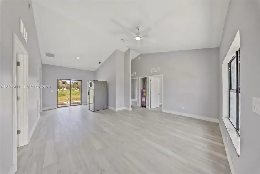 Open-concept interior featuring vaulted ceilings, wood-finish flooring, a ceiling fan, and sliding glass doors