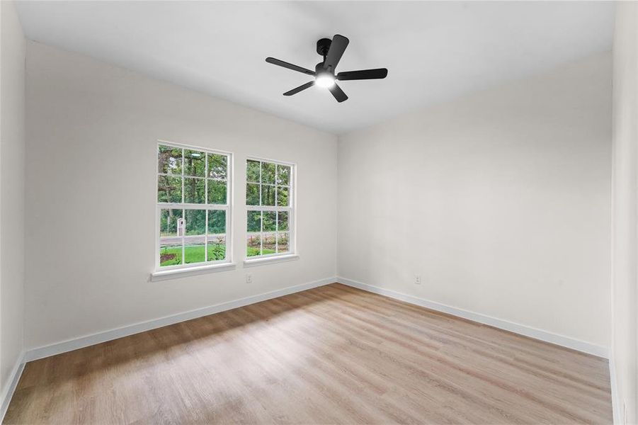 Bright interior featuring wood-finish flooring, white walls, and a modern ceiling fan Bright interior featuring wood-finish flooring, white walls, and a modern ceiling fan