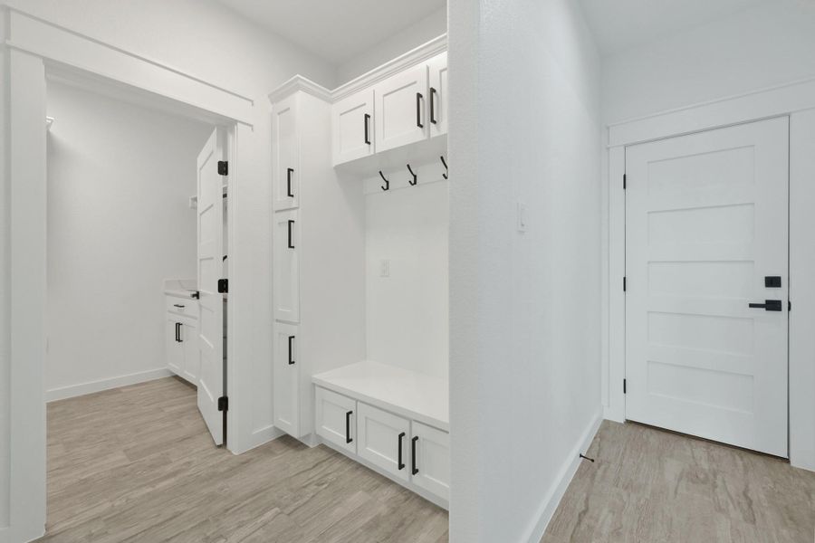 Mudroom featuring built-in cabinetry with matte black hardware, integrated bench seating, and wall-mounted hooks