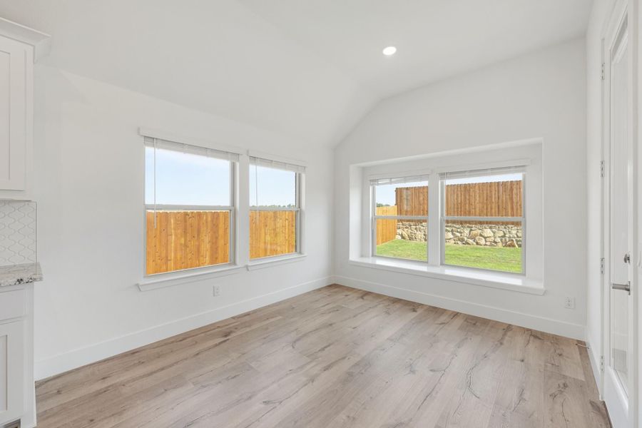 Empty dining area with vaulted ceiling, light wood floors, and large windows overlooking backyard fence. Empty dining area with vaulted ceiling, light wood floors, and large windows overlooking backyard fence.