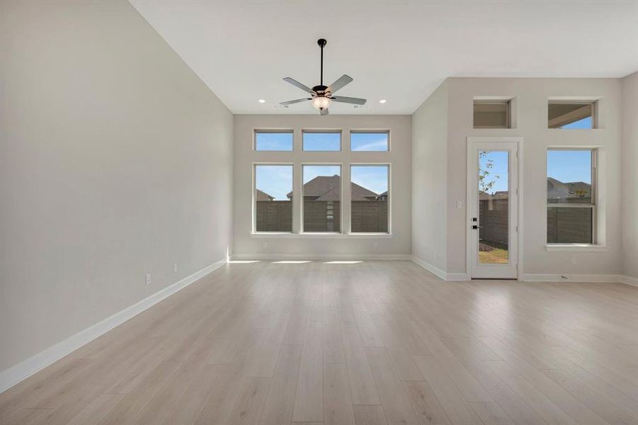 Spacious room featuring high ceilings, wood-finish flooring, a contemporary ceiling fan, multiple large windows, and a glass-paneled exterior door
