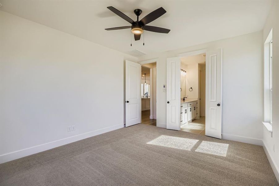 Unfurnished bedroom with light colored carpet, ceiling fan, and ensuite bath Unfurnished bedroom with light colored carpet, ceiling fan, and ensuite bath