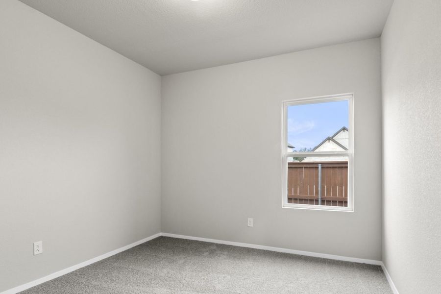 Image of a bedroom with tan carpeting and light grey walls with a window