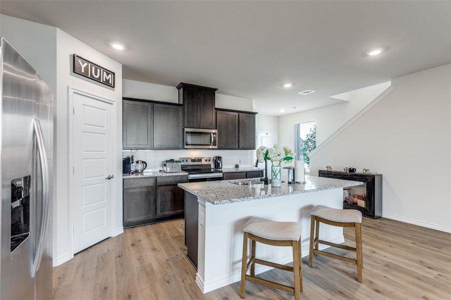 Kitchen featuring appliances with stainless steel finishes, light wood finished floors, a kitchen island with sink, a breakfast bar area, and light stone countertops Kitchen featuring appliances with stainless steel finishes, light wood finished floors, a kitchen island with sink, a breakfast bar area, and light stone countertops