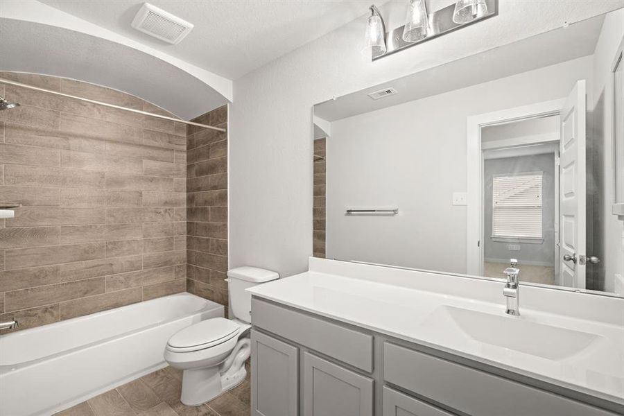 Secondary bath features tile flooring, bath/shower combo with tile surround, light stained wood cabinets, beautiful light countertop. Sample photo of completed home with similar floor plan. As-built interior colors and selections may vary.