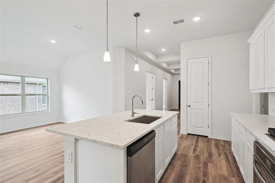 Kitchen with white cabinetry, stainless steel appliances, sink, wood-type flooring, and a center island with sink