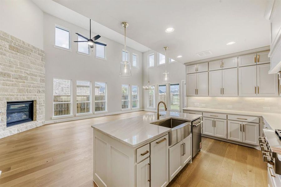 Kitchen with a kitchen island with sink, a stone fireplace, light wood-type flooring, open floor plan, and light stone counters