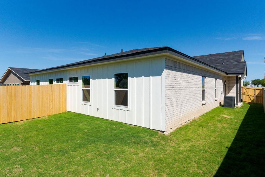 View of side of property with board and batten siding, a fenced backyard, brick siding, and a gate