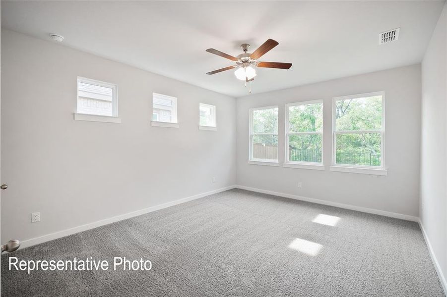 This room features light gray walls, gray carpeting, a ceiling fan with light fixture, and a series of windows that provide natural illumination