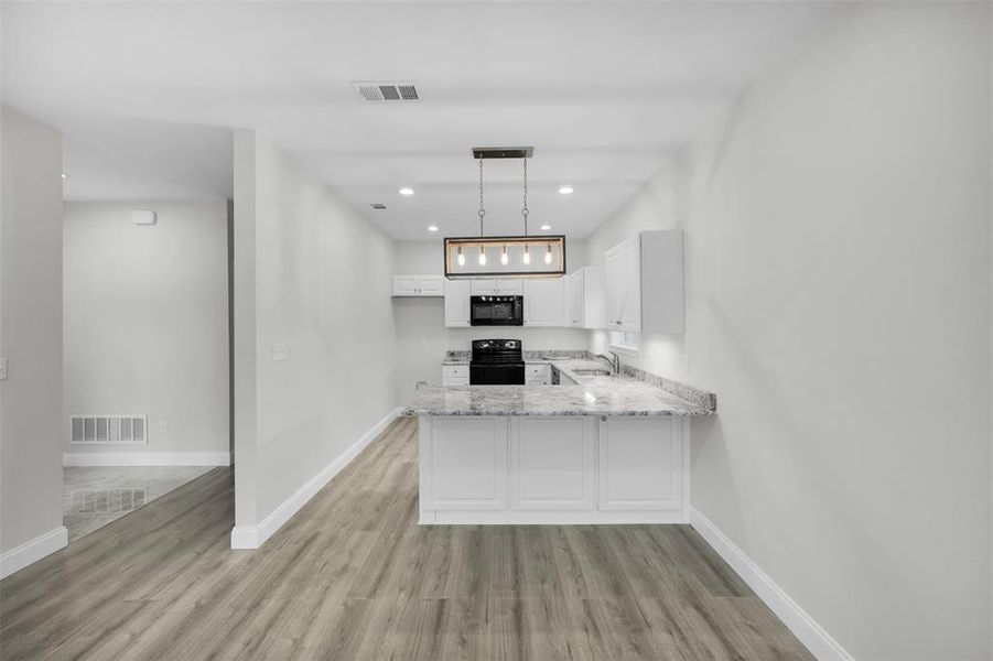Kitchen with a peninsula, white cabinetry, black appliances, and visible vents Kitchen with a peninsula, white cabinetry, black appliances, and visible vents