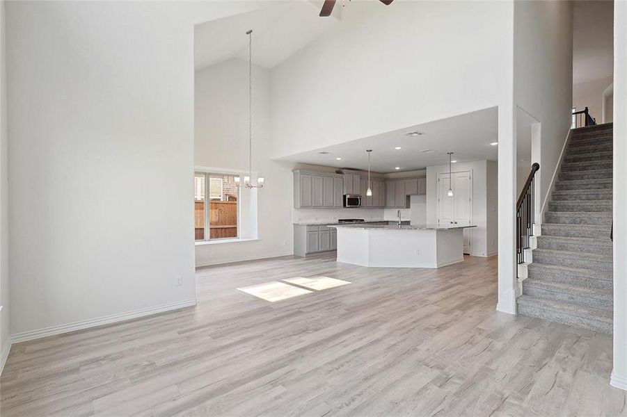 Unfurnished living room with high vaulted ceiling, light wood-type flooring, and ceiling fan with notable chandelier