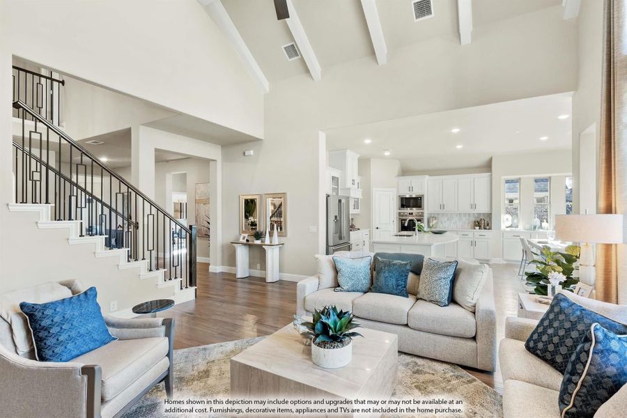 Open-concept living room with vaulted beamed ceiling, staircase, and white kitchen visible in background Open-concept living room with vaulted beamed ceiling, staircase, and white kitchen visible in background