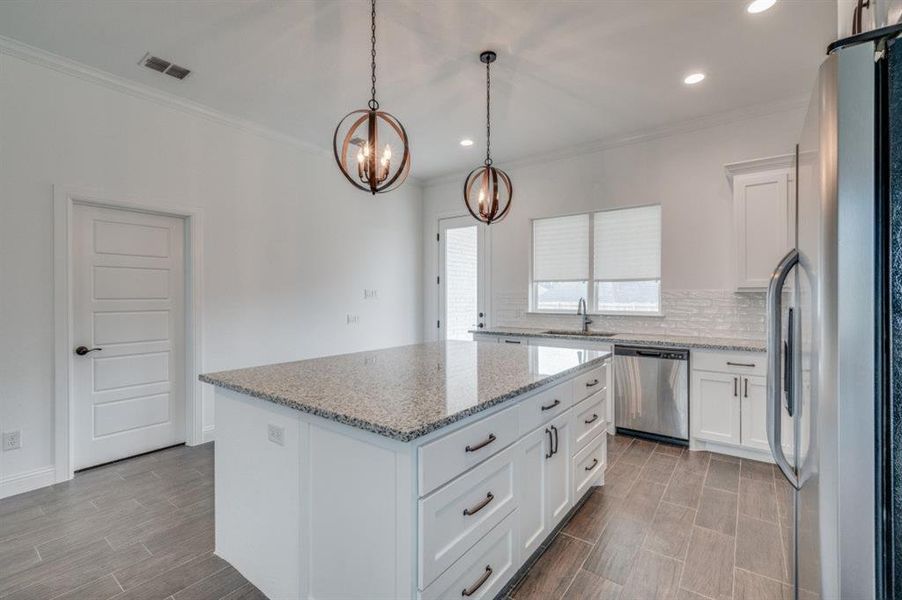 Kitchen with white cabinets, a center island, stainless steel dishwasher, and refrigerator