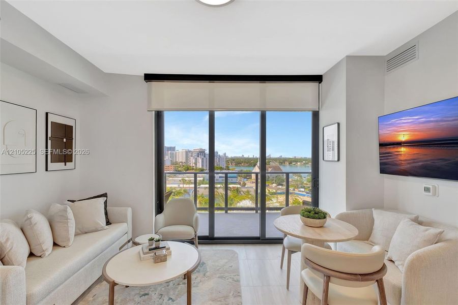 Floor-to-ceiling glass doors opening to a balcony, light-toned wall finishes, recessed ceiling lighting, and a wall-mounted flat-screen display