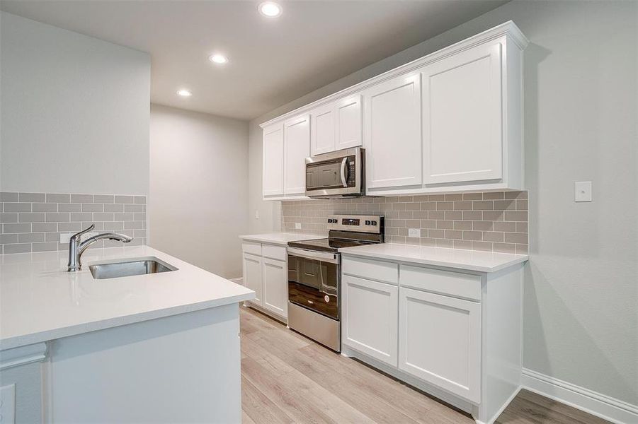 Kitchen featuring appliances with stainless steel finishes, sink, white cabinets, and light hardwood / wood-style flooring