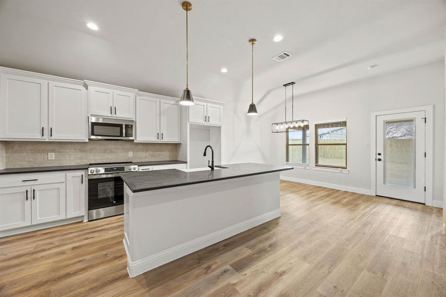 Kitchen with appliances with stainless steel finishes, an island with sink, backsplash, white cabinets, and recessed lighting