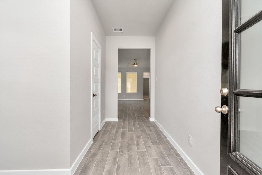Greeted by a elegant glass front door, the entrance beckons with high ceilings, adorned with elegant wood-look tile flooring and oversized baseboards. Sample photo of completed home with similar floor plan. As-built interior colors and selections may vary.