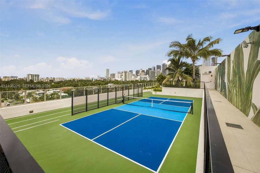 Rooftop pickleball court featuring a multi-color high-performance surface, glass perimeter fencing, integrated track markings, and mural-style wall accents Rooftop pickleball court featuring a multi-color high-performance surface, glass perimeter fencing, integrated track markings, and mural-style wall accents