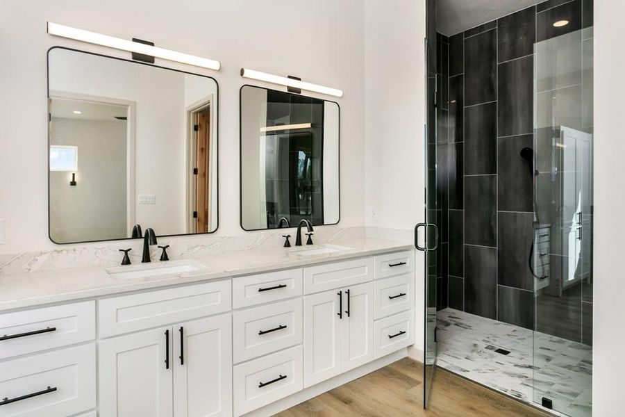Full bathroom featuring double vanity, light wood-style floors, and a stall shower Full bathroom featuring double vanity, light wood-style floors, and a stall shower