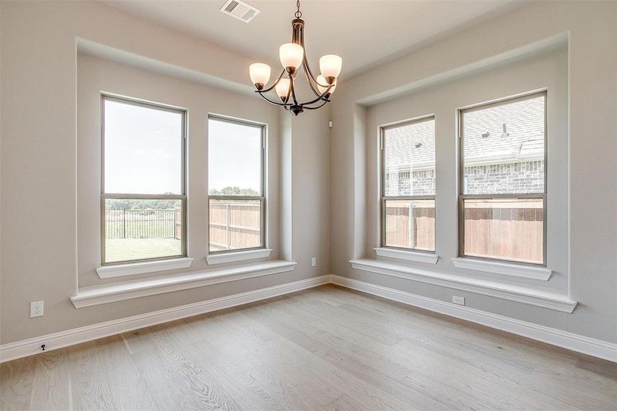 Empty room featuring a chandelier, light hardwood / wood-style floors, and a healthy amount of sunlight