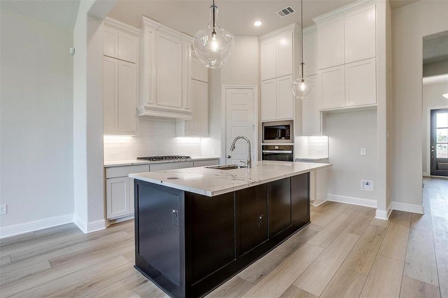 Kitchen with white cabinets, sink, light stone countertops, an island with sink, and stainless steel appliances