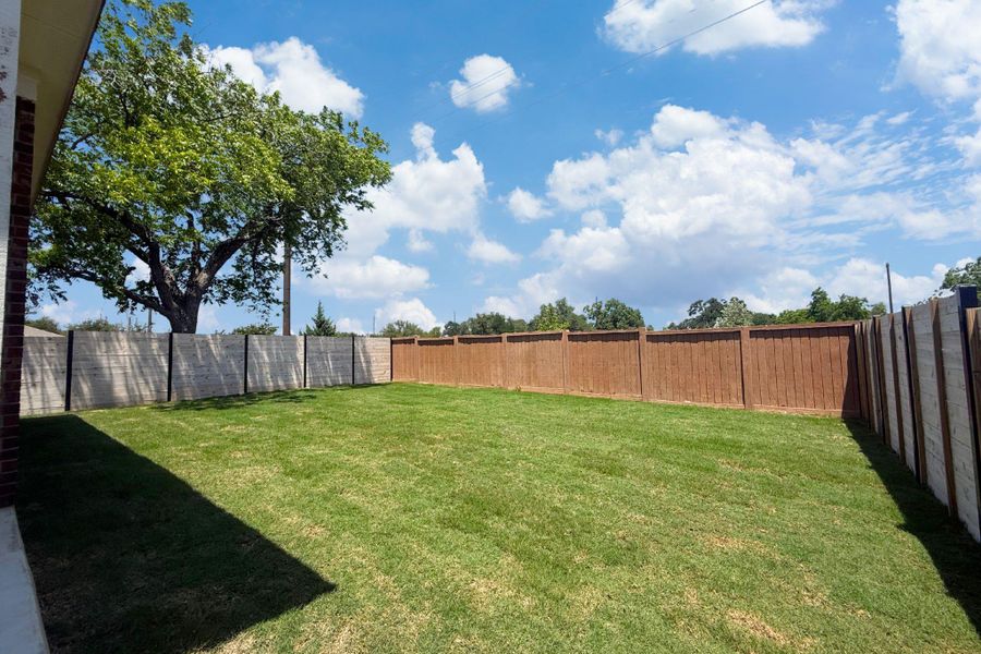 Expansive rear yard featuring natural grass, a mature tree, and a combination of wood and composite fencing