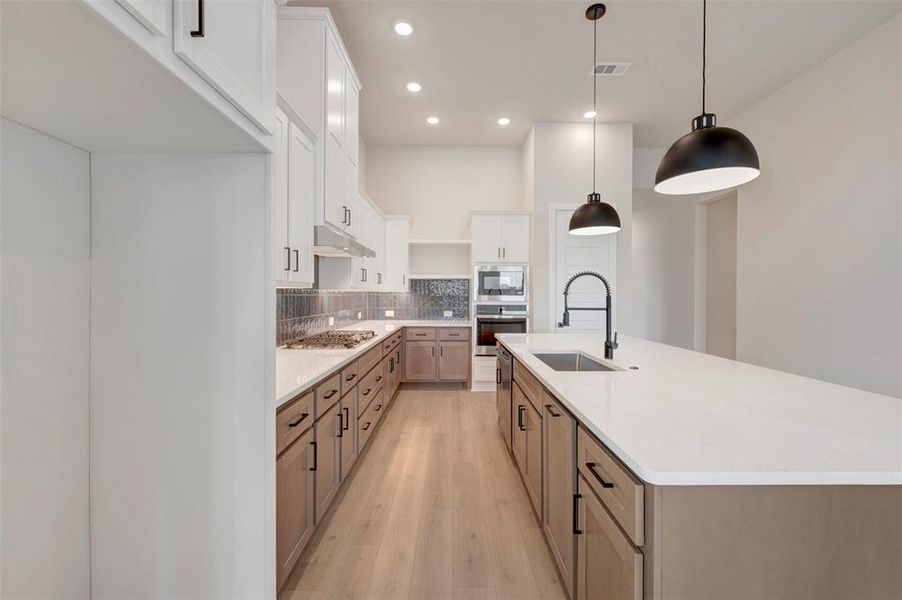 Kitchen with two tone cabinets, a spacious island, light wood-type flooring, decorative backsplash, and decorative light fixtures