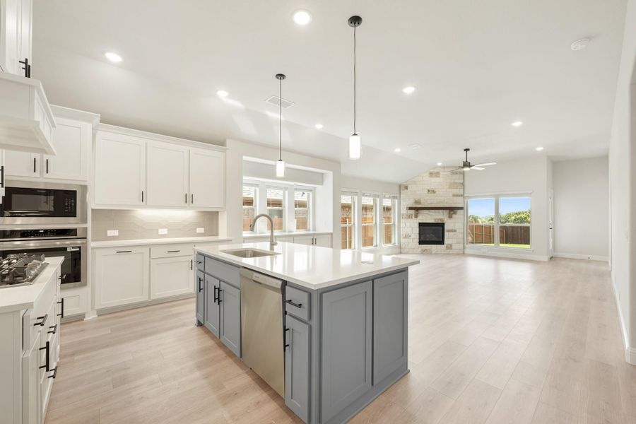 Open kitchen with gray island, white cabinets, and light wood floors opening to living room with stone fireplace