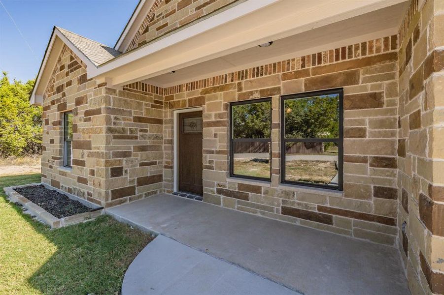 View of exterior entry with brick siding, stone siding, and roof with shingles