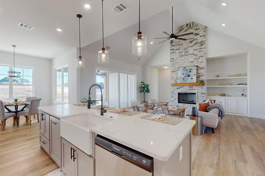 Kitchen with dishwasher, light stone counters, a center island with sink, built in shelves, and decorative light fixtures