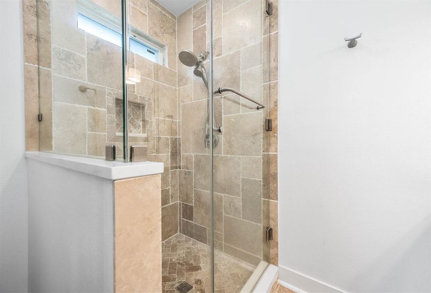 The primary shower features elegant floor-to-ceiling tile work, a sleek glass enclosure, and a built-in storage niche for added convenience. The modern design and clean finishes create a spa-like feel within the primary bath.