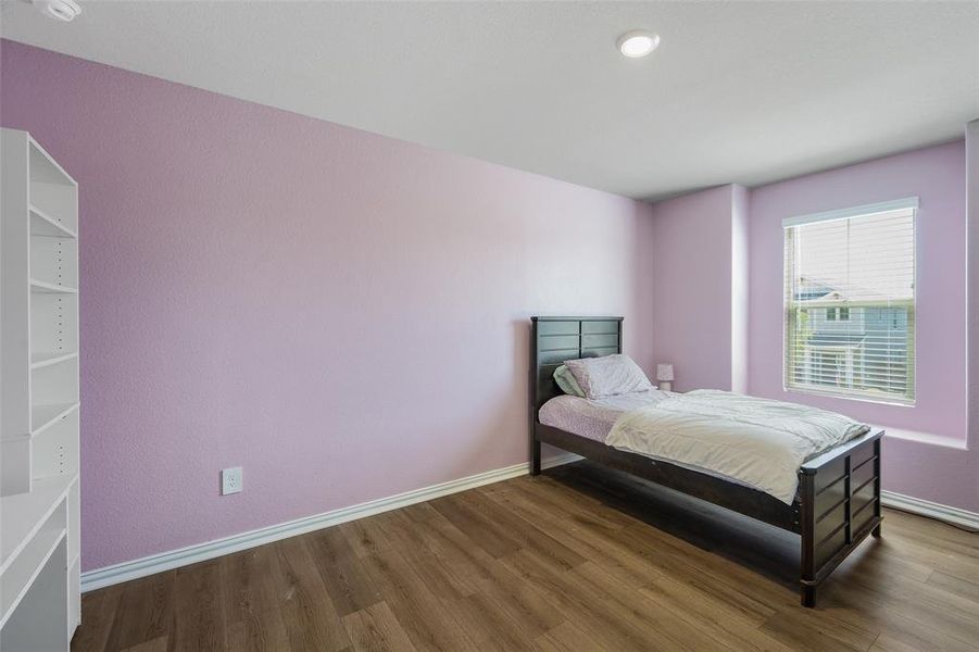 Bedroom featuring wood-finish flooring, a built-in shelving unit, a window with blinds, and recessed lighting Bedroom featuring wood-finish flooring, a built-in shelving unit, a window with blinds, and recessed lighting
