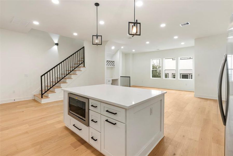 You're looking at a bright, modern kitchen with sleek white cabinetry and stainless steel appliances, complemented by warm hardwood floors. The space opens to a living area with large windows for natural lighting.