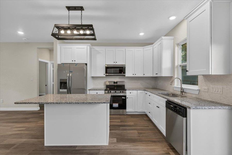 White shaker cabinetry, granite countertops, and wood-look flooring define this modern cooking space. White shaker cabinetry, granite countertops, and wood-look flooring define this modern cooking space.