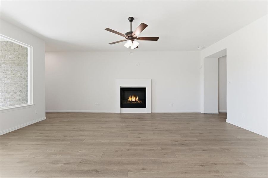 Unfurnished living room featuring a glass covered fireplace, light wood-style flooring, and ceiling fan