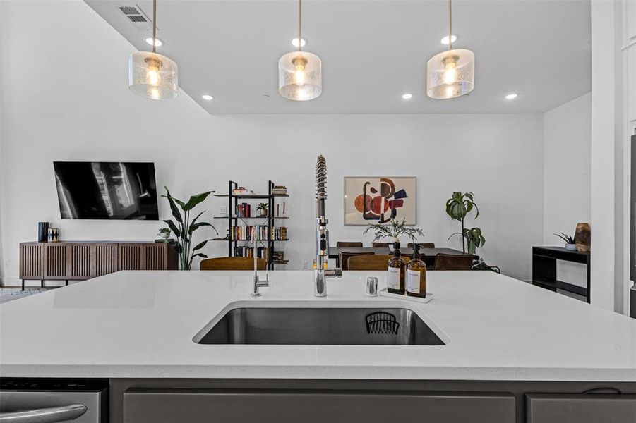 Kitchen with decorative light fixtures, light stone countertops, stainless steel dishwasher, recessed lighting, and an island with sink