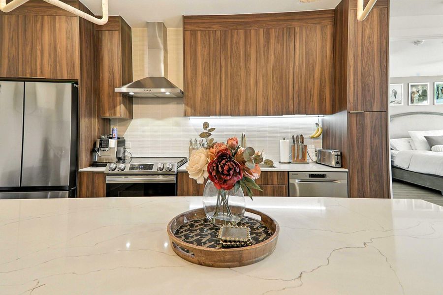 Kitchen featuring modern cabinets, appliances with stainless steel finishes, wall chimney exhaust hood, brown cabinetry, and backsplash