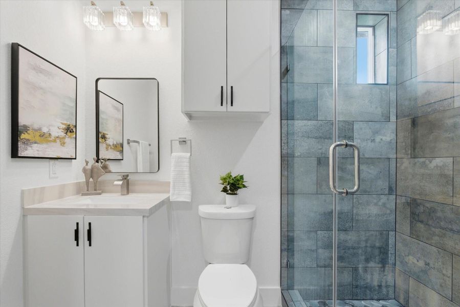 Moody gray and blue tones define this hall bathroom, featuring a modern exposed shower system, an enclosed glass shower, and soft natural light streaming through a peekaboo window.