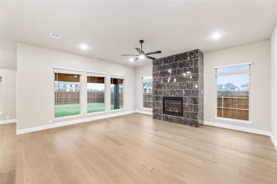 Open living room with hardwood floors, ceiling fan, and floor-to-ceiling dark stone fireplace surround