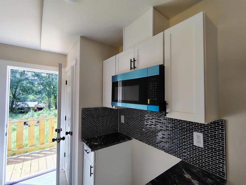 Kitchen with stainless steel microwave, decorative backsplash, white cabinets, and dark stone counters