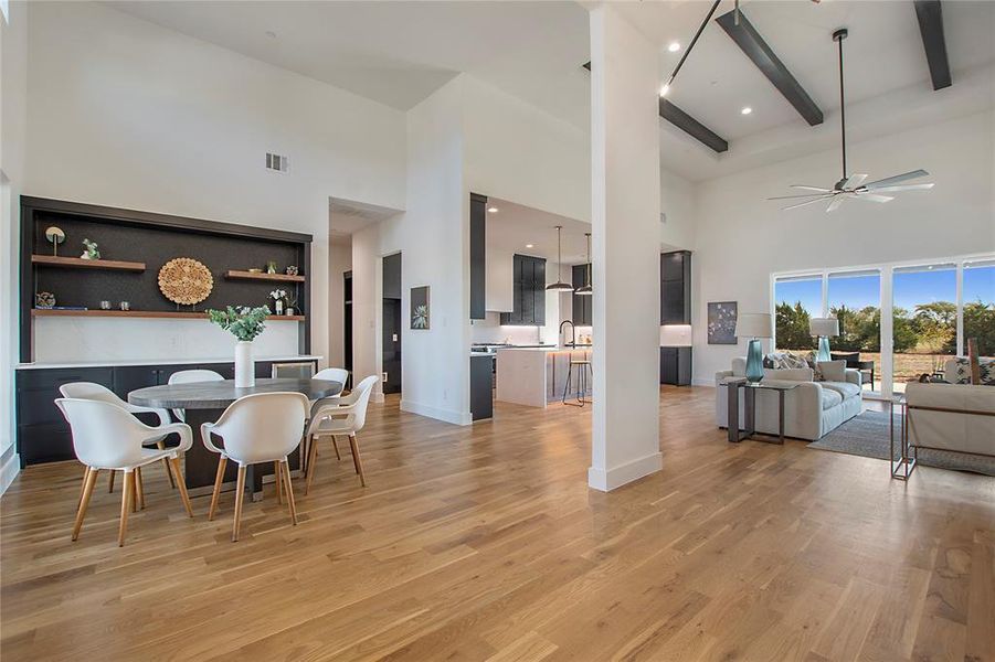 Spacious open-concept living area featuring high vaulted ceilings with exposed beams, wood-finish flooring, and large windows Spacious open-concept living area featuring high vaulted ceilings with exposed beams, wood-finish flooring, and large windows