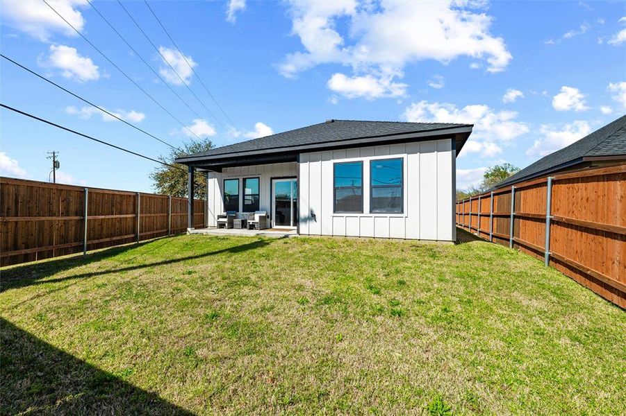 Rear view of property featuring board and batten siding, a patio, a fenced backyard, and a shingled roof