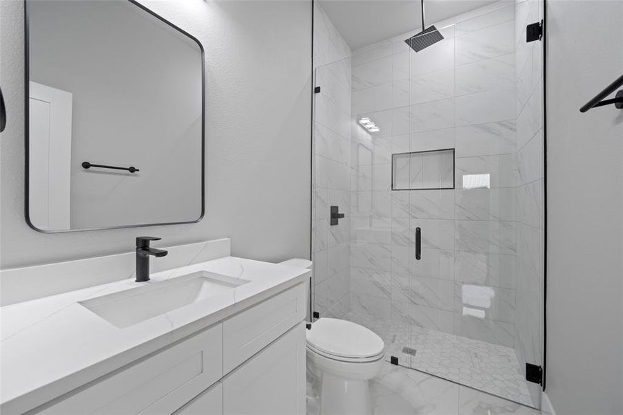 Full bath featuring vanity, toilet, marble finish floor, and a stall shower