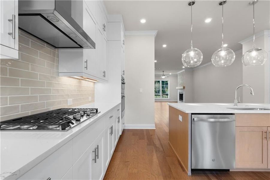 Kitchen featuring wall chimney range hood, dark wood-type flooring, appliances with stainless steel finishes, white cabinetry, and light stone countertops