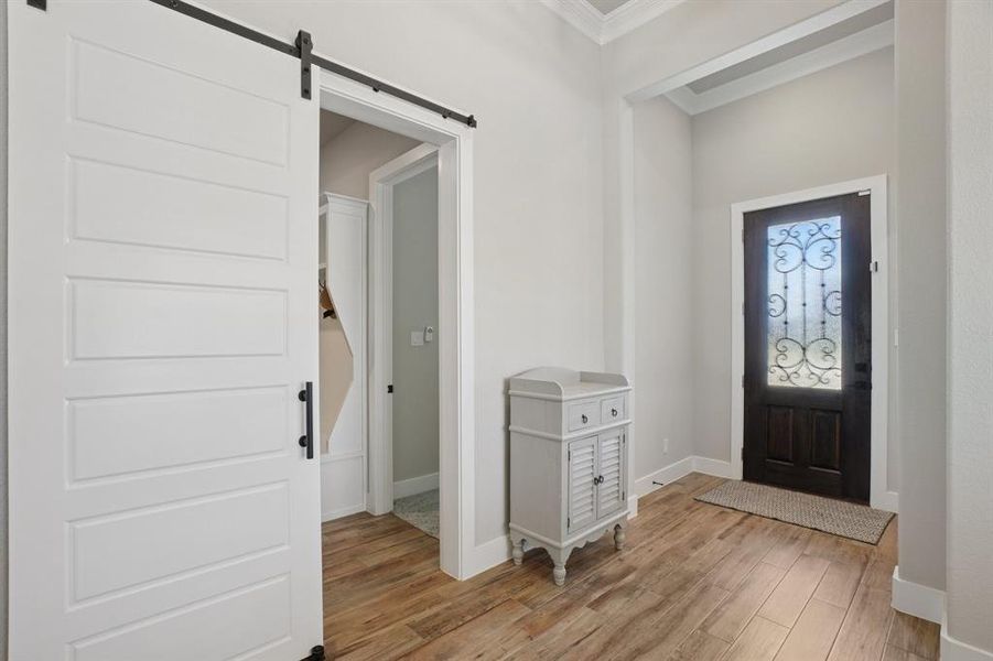 Foyer featuring light wood-look ceramic flooring, a barn door, and ornamental molding