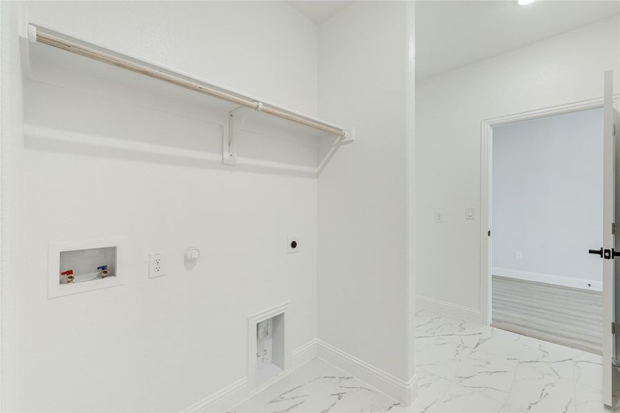 Laundry room with built-in shelf, washer and dryer hookups, and marble-look tile floors