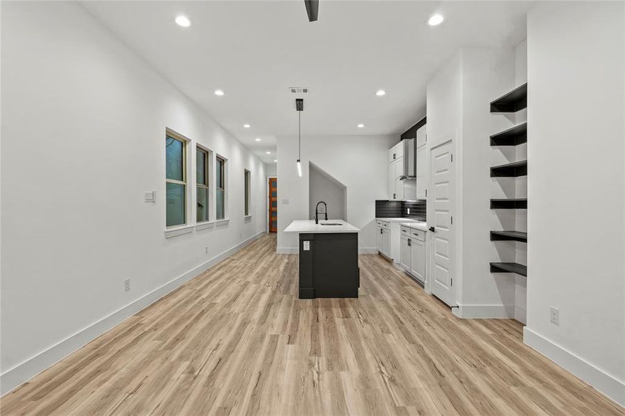 Kitchen with pendant lighting, a center island with sink, white cabinets, sink, and light hardwood / wood-style floors