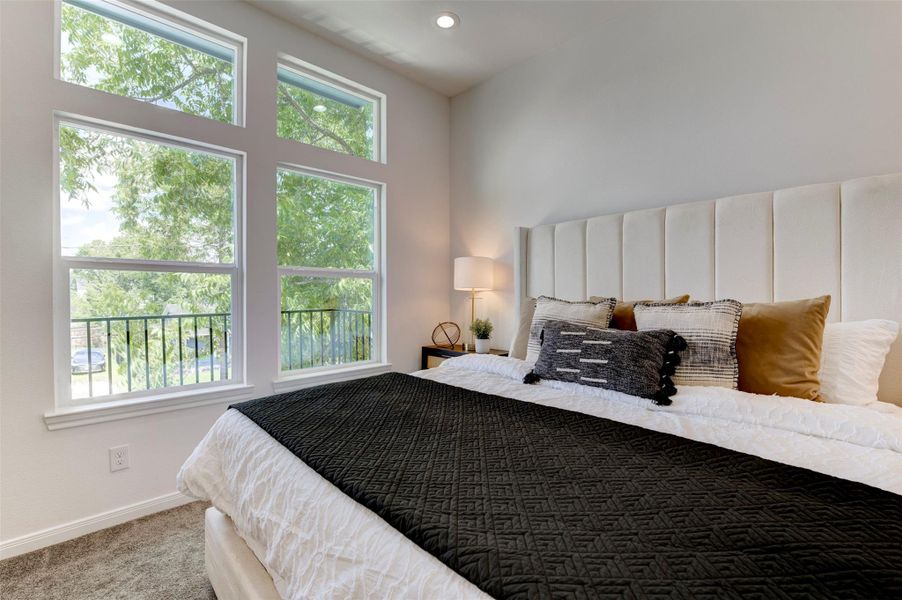 Primary bedroom with floor-to-ceiling windows, balcony view, recessed lighting, and carpet flooring.