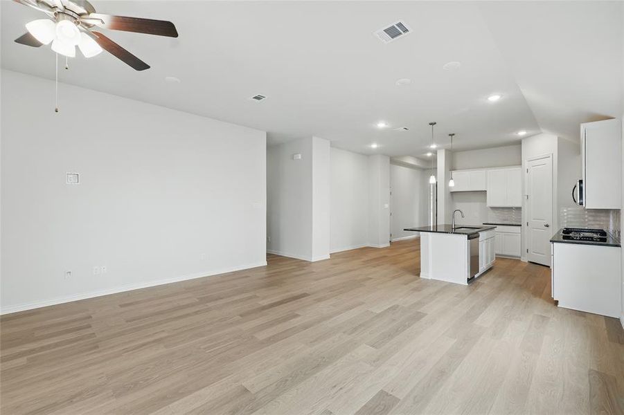 Kitchen with open floor plan, an island with sink, white cabinetry, light wood-style floors, and a ceiling fan