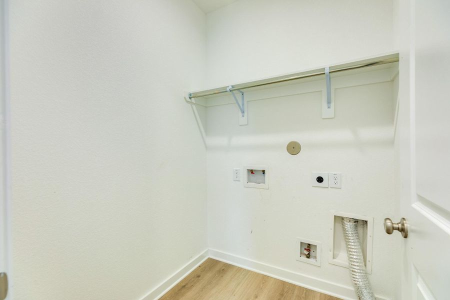 This spacious laundry room is conveniently situated at the front of the home and features a built-in garment rack, complemented by extensive storage shelving.